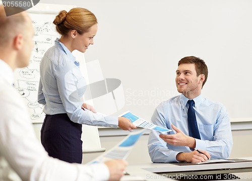 Image of smiling woman giving papers to man in office