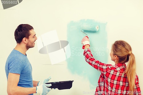 Image of smiling couple painting wall at home