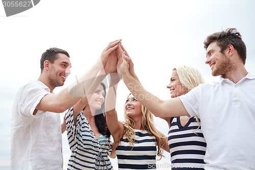 Image of smiling friends making high five gesture outdoors