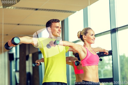 Image of smiling man and woman with dumbbells in gym