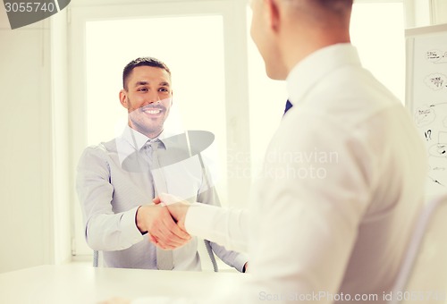 Image of two smiling businessmen shaking hands in office
