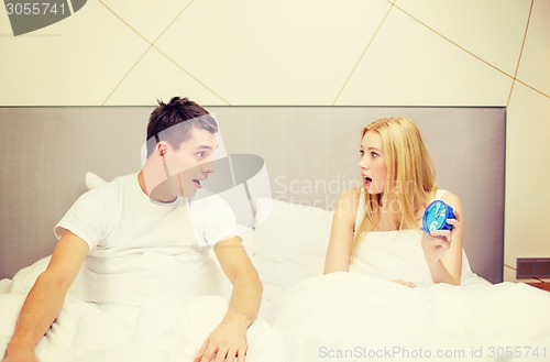 Image of surprised couple with clock in bed