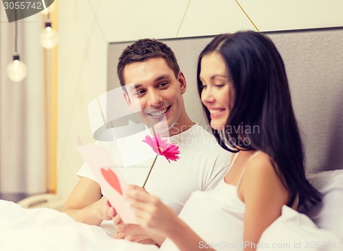 Image of smiling couple in bed with postcard and flower