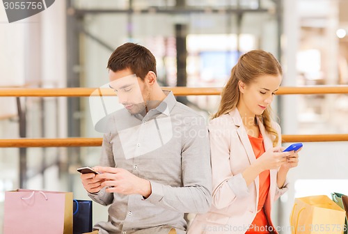 Image of couple with smartphones and shopping bags in mall