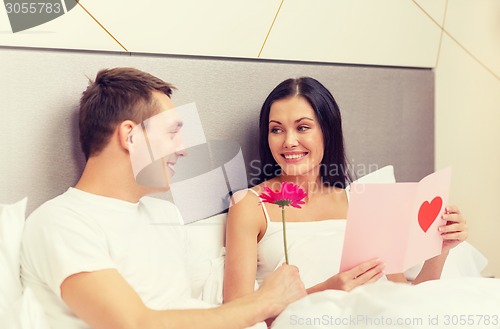 Image of smiling couple in bed with postcard and flower