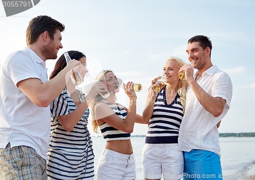 Image of smiling friends with drinks in bottles on beach