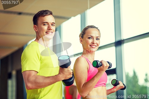 Image of smiling man and woman with dumbbells in gym