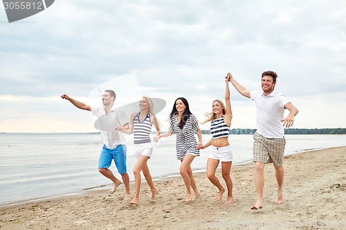 Image of smiling friends in sunglasses running on beach