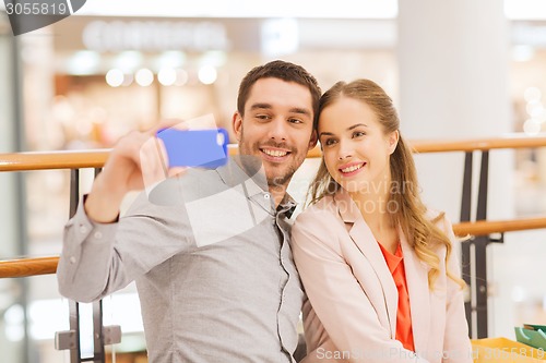 Image of happy couple with smartphone taking selfie in mall