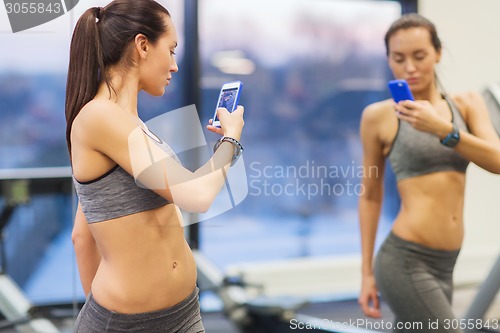 Image of woman with smartphone taking mirror selfie in gym