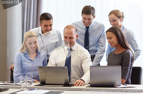 Image of smiling businesspeople with laptops in office