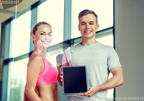 Image of smiling young woman with personal trainer in gym