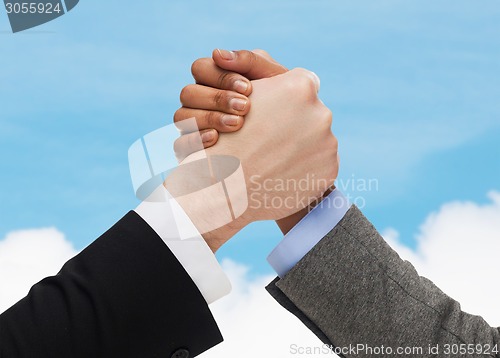 Image of close up of hands arm wrestling over concrete wall