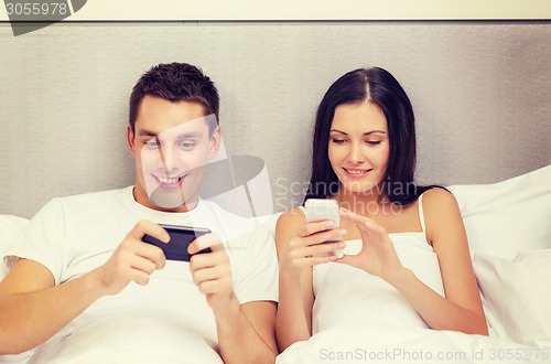 Image of smiling couple in bed with smartphones