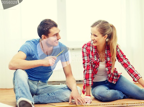 Image of smiling couple measuring wood flooring