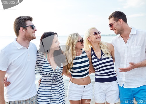 Image of smiling friends in sunglasses talking on beach