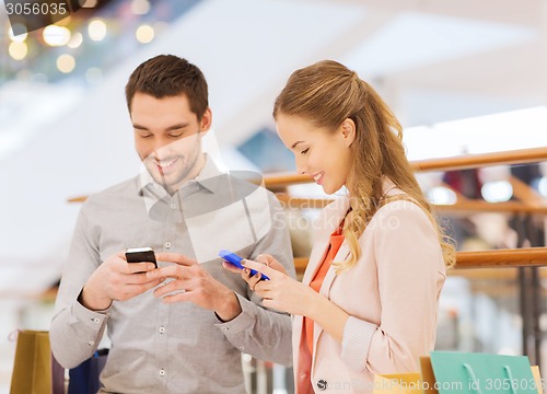 Image of couple with smartphones and shopping bags in mall