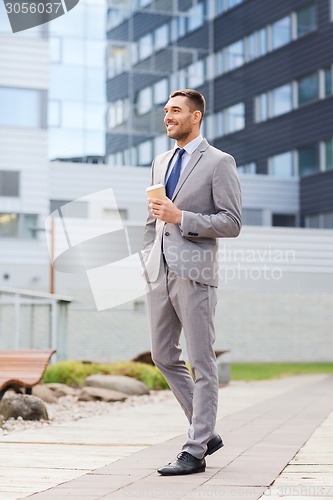 Image of young serious businessman with paper cup outdoors