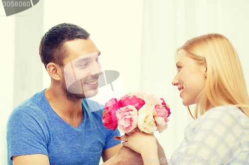 Image of smiling man giving girfriens flowers at home