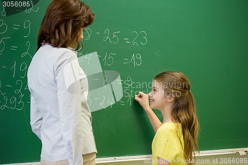 Image of little smiling schoolgirl writing on chalk board