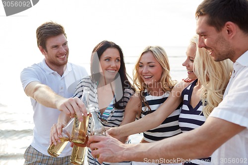 Image of smiling friends clinking bottles on beach