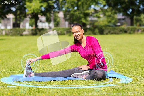 Image of smiling woman stretching leg on mat outdoors