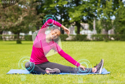 Image of smiling woman stretching leg on mat outdoors