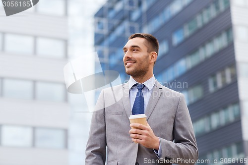 Image of young smiling businessman with paper cup outdoors
