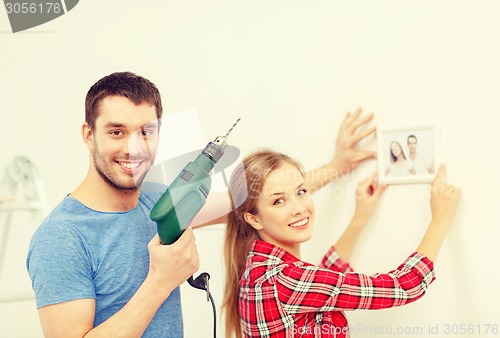 Image of smiling couple drilling hole in wall at home