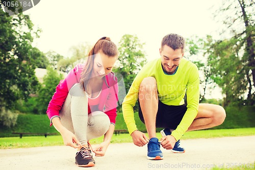 Image of smiling couple tying shoelaces outdoors