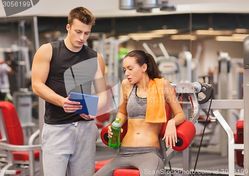 Image of smiling young woman with personal trainer in gym