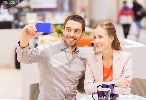 Image of happy couple with smartphone taking selfie in mall