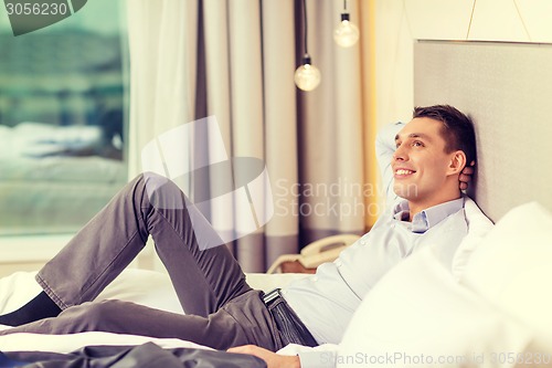 Image of happy businesswoman lying in bed in hotel room