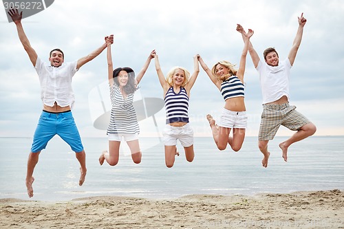 Image of smiling friends in sunglasses walking on beach