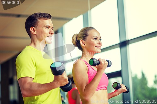 Image of smiling man and woman with dumbbells in gym