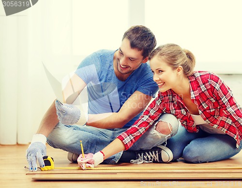 Image of smiling couple measuring wood flooring