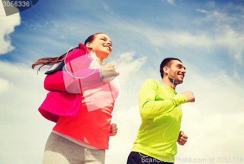 Image of smiling couple with earphones running outdoors