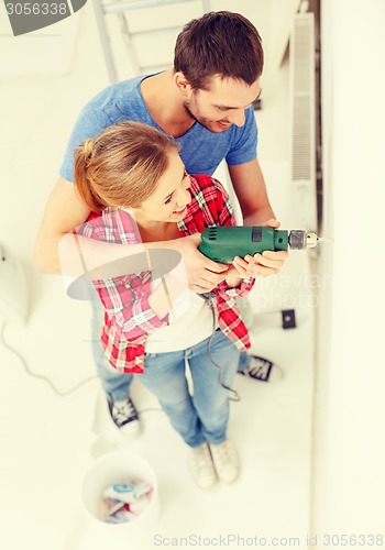 Image of smiling couple drilling hole in wall at home