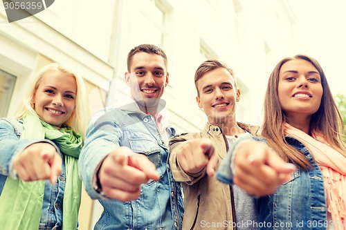 Image of group of smiling friends in city pointing finger