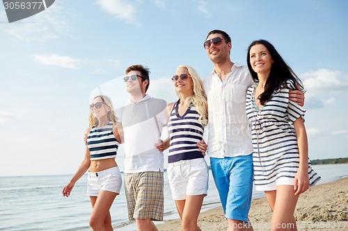 Image of smiling friends in sunglasses walking on beach