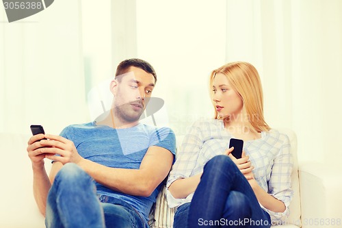 Image of concentrated couple with smartphones at home