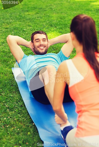 Image of smiling man doing exercises on mat outdoors
