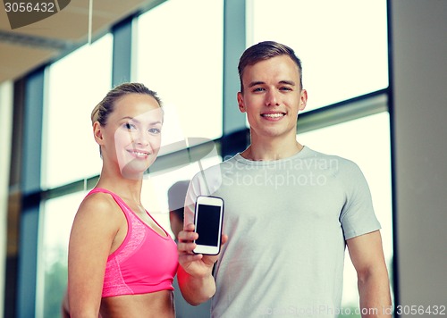 Image of smiling young woman with personal trainer in gym