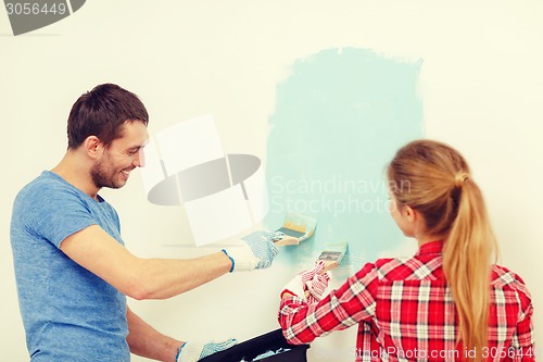 Image of smiling couple painting wall at home