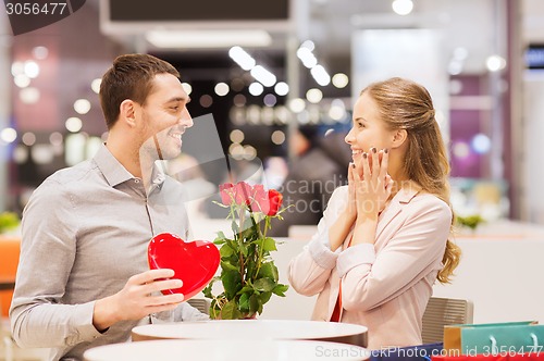 Image of happy couple with present and flowers in mall