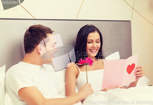 Image of smiling couple in bed with postcard and flower