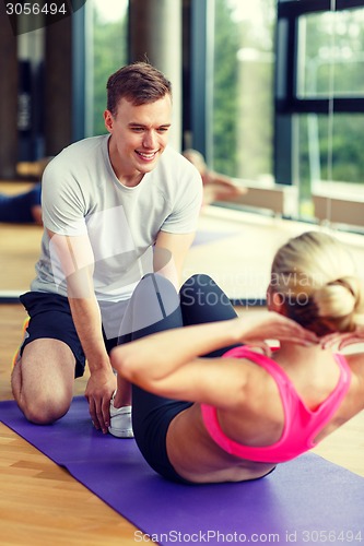 Image of smiling woman with male trainer exercising in gym