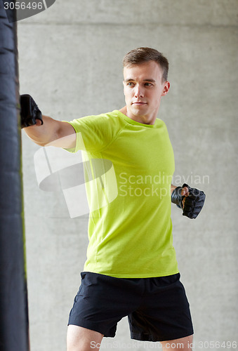 Image of young man in gloves boxing with punching bag