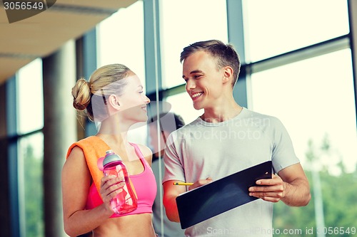 Image of smiling young woman with personal trainer in gym