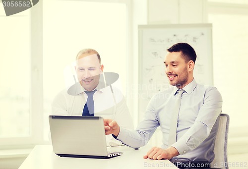 Image of two smiling businessmen with laptop in office